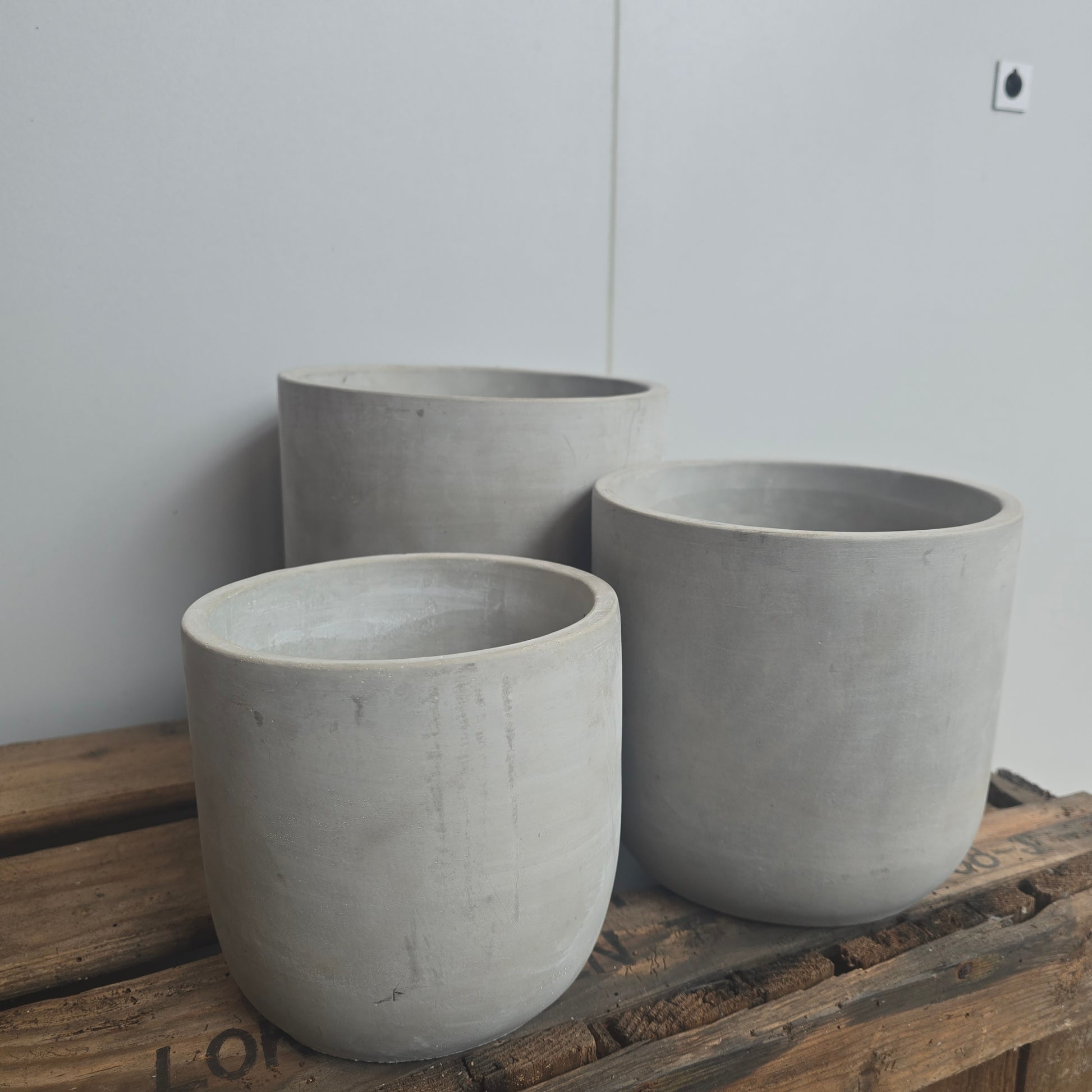 Een collectie cementkleurige potten voor kamerplanten met verschillende diameters uit een ander perspectief